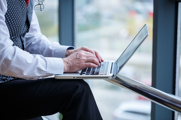 Homem de negócios adulto, professor, mentor trabalhando em um novo projeto. Senta-se junto a uma grande janela sobre a mesa. Ele olha para a tela do laptop.