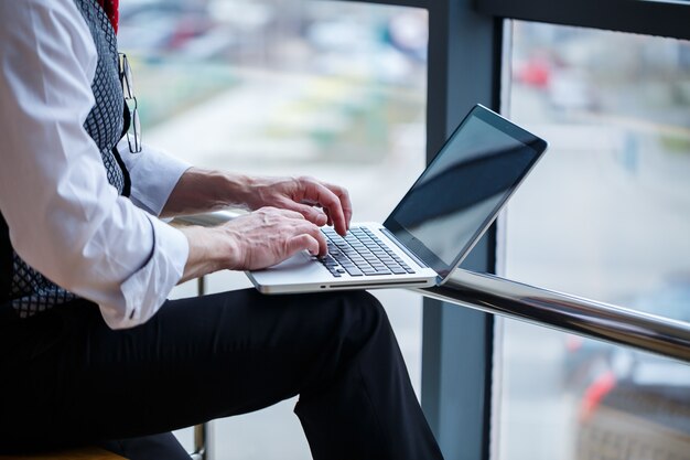 Homem de negócios adulto, professor, mentor trabalhando em um novo projeto. Senta-se junto a uma grande janela sobre a mesa. Ele olha para a tela do laptop.