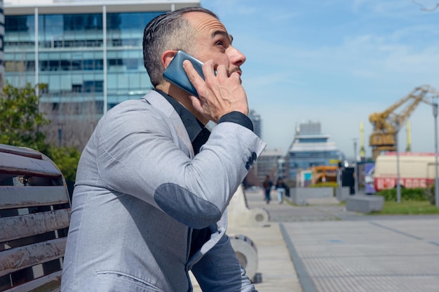 homem de negócios adulto sentado ao ar livre falando ao telefone olhando para o céu e pensativo