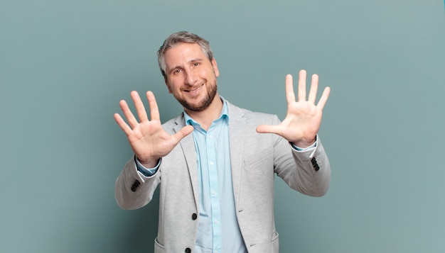 Homem de negócios adulto sorrindo e parecendo amigável, mostrando o número dez ou décimo com a mão para a frente, em contagem regressiva