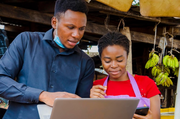 Homem de negócios africano jovem se sente animado enquanto mostra a uma mulher do mercado algumas informações em seu laptop.