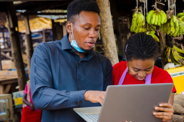 Homem de negócios africano jovem se sente animado enquanto mostra a uma mulher do mercado algumas informações em seu laptop.