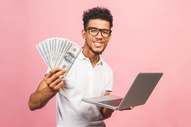 Homem de negócios afro-americano ganhando dinheiro com a internet, segurando dinheiro na mão e laptop em outra