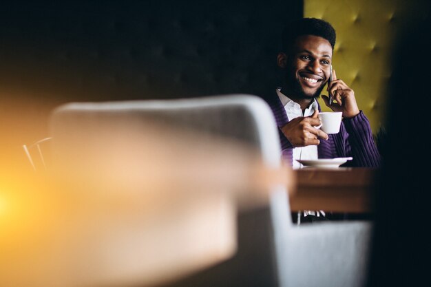 Homem de negócios americano africano com telefone e café em um café