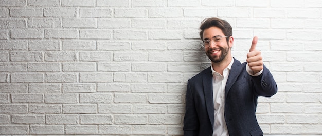 Homem de negócios amigável jovem alegre e animado, sorrindo e levantando o dedo, conceito de sucesso e aprovação, ok gesto