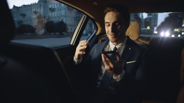 Foto homem de negócios animado compartilhando boas notícias em mensagem de voz no telefone no carro escuro