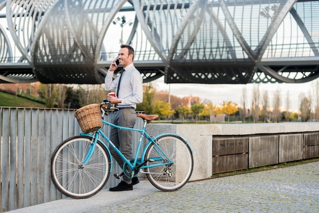 Homem de negócios ao lado de sua bicicleta vintage falando no celular