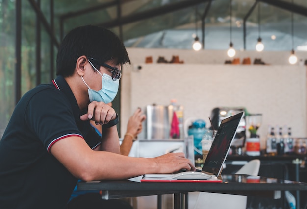 Homem de negócios asiático casual usa máscara facial e analisa dados de preços de negociação do mercado de ações on-line em um laptop