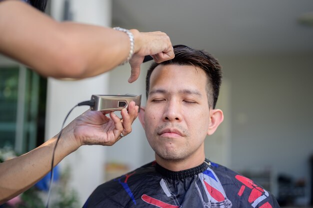 Homem de negócios asiático fazendo corte de cabelo e salão de beleza em casa. Barbearia ao ar livre no jardim. Distanciamento social e novo estilo de vida normal.