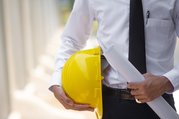 Homem de negócios asiático segurando capacete na construção do local