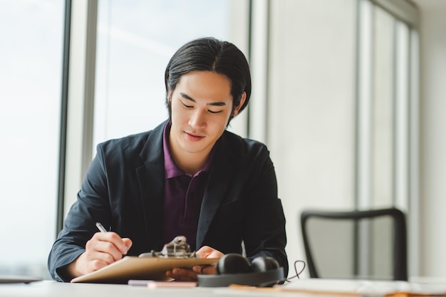 Homem de negócios asiático tomando notas sentado no local de trabalho em um escritório moderno