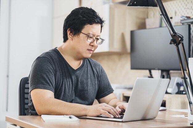 Homem de negócios asiático usando laptop de tecnologia para trabalhar em casa em um quarto interno