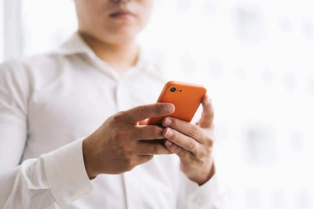 Homem de negócios asiático usando smartphone perto da janela