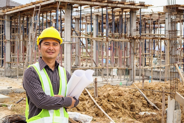 Homem de negócios asiáticos engenheiro de construção trabalhador com capacete protetor e projetos de papel disponível no local de construção da casa