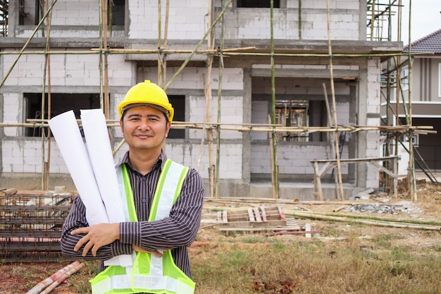 Homem de negócios asiáticos engenheiro de construção trabalhador com capacete protetor e projetos de papel disponível no local de construção da casa