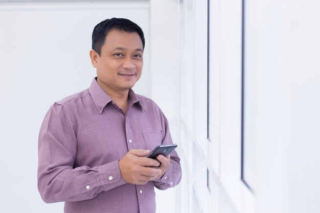 Homem de negócios asiáticos está segurando um smartphone na mão e olha pela janela