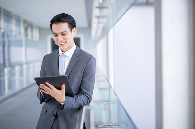 Homem de negócios asiáticos jovem segurando um tablet olhando para longe, conceito de negócio inteligente.