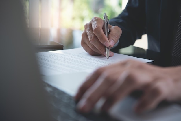 Homem de negócios, assinando o documento formal do contrato oficial e usando o computador portátil no escritório