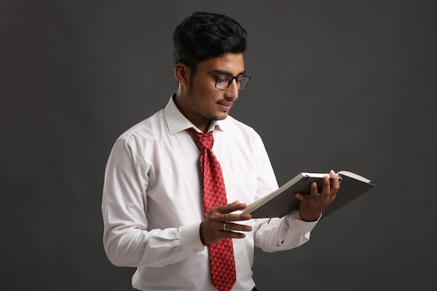 Foto homem de negócios bem sucedido indiano jovem ou executivo usando óculos e lendo o livro sobre fundo escuro.