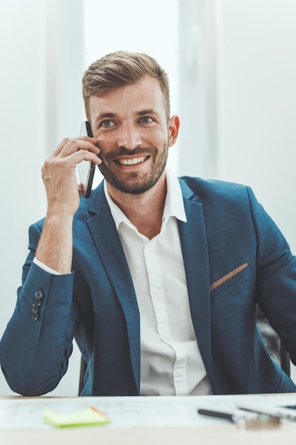 Homem de negócios bem sucedido jovem falando no smartphone enquanto trabalhava em um novo projeto no escritório.