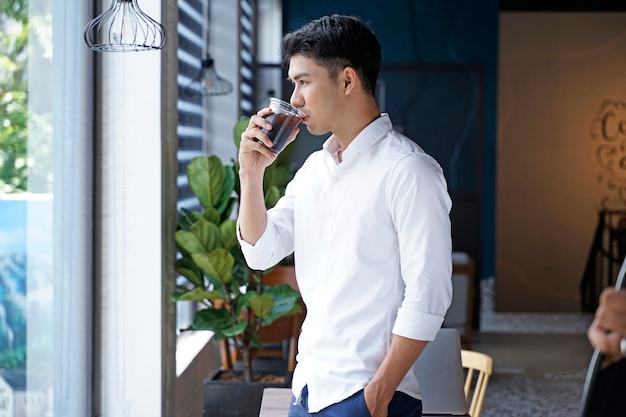 Homem de negócios bonito asiático ou trabalhador de escritório ou jovem estudante tomando café em uma cafeteria