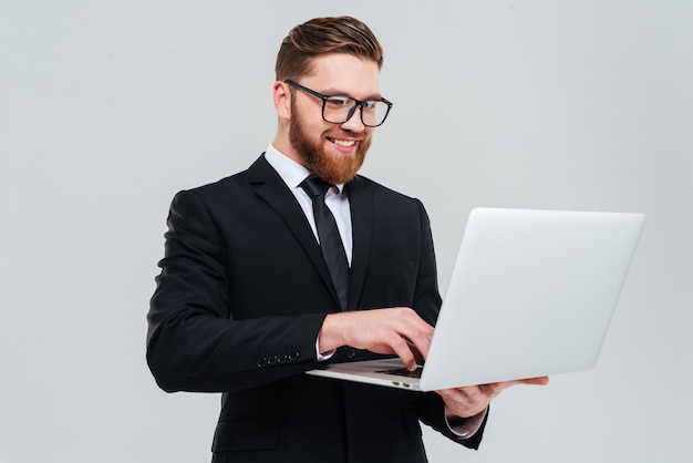 Homem de negócios bonito de óculos e terno segurando laptop nas mãos e escrevendo algo.