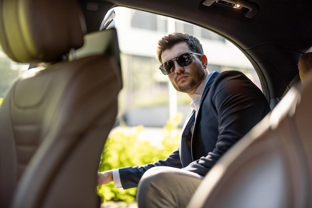 Homem de negócios bonito entrando no carro no banco de trás de um táxi de luxo veículo de transporte e conceito de estilo de vida de negócios