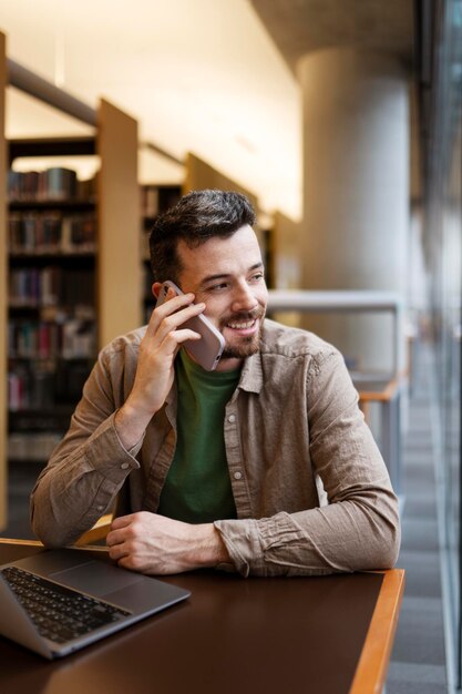 Homem de negócios bonito falando no celular sentado no local de trabalho Freelancer sorridente usando laptop