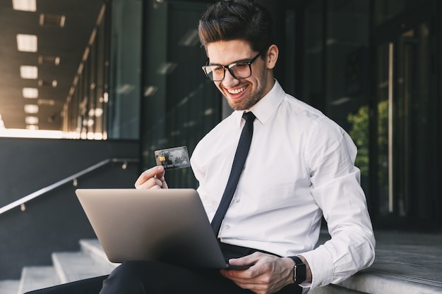 Homem de negócios bonito perto do centro de negócios, usando o computador portátil.