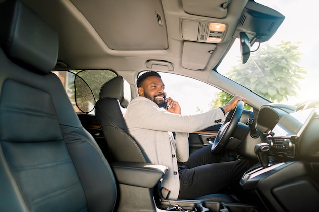 Homem de negócios bonito preto dirigindo o carro falando no smartphone.