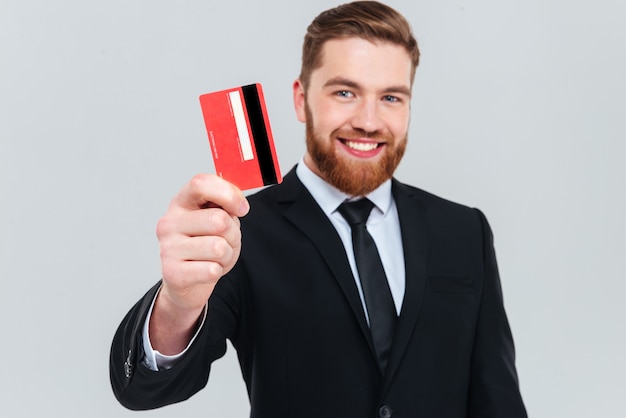 Homem de negócios bonito sorridente de terno preto segurando o cartão de crédito