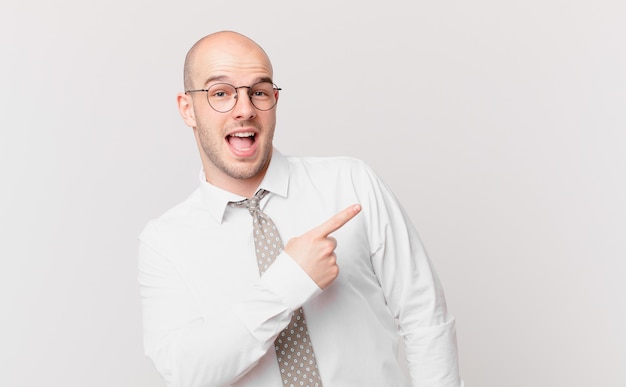 Homem de negócios careca parecendo animado e surpreso apontando para o lado e para cima para copiar o espaço