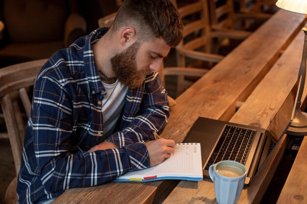 Homem de negócios casuais ou freelancer planejando seu trabalho no notebook, trabalhando no computador portátil com um telefone inteligente, xícara de café na mesa da cafeteria ou escritório em casa.