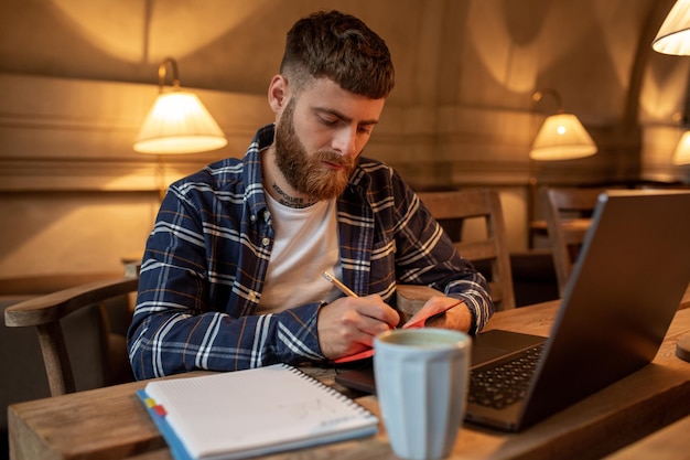 Foto homem de negócios casuais ou freelancer planejando seu trabalho no notebook, trabalhando no computador portátil com um telefone inteligente, xícara de café na mesa da cafeteria ou escritório em casa.