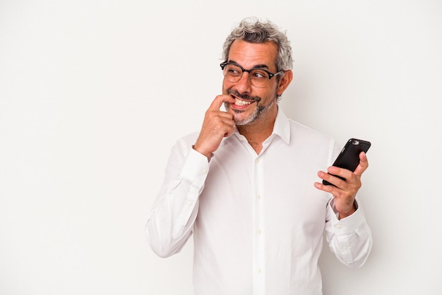 Homem de negócios caucasiano de meia-idade segurando um telefone celular isolado no fundo branco relaxado pensando em algo olhando para um espaço de cópia