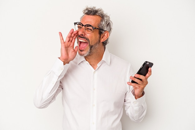 Homem de negócios caucasiano de meia-idade, segurando um telefone móvel isolado no fundo branco, gritando e segurando a palma da mão perto da boca aberta.