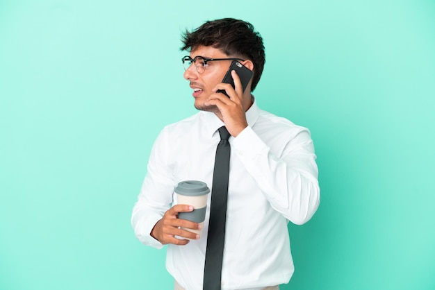 Homem de negócios, caucasiano, isolado em um fundo azul, segurando um café para levar e um celular