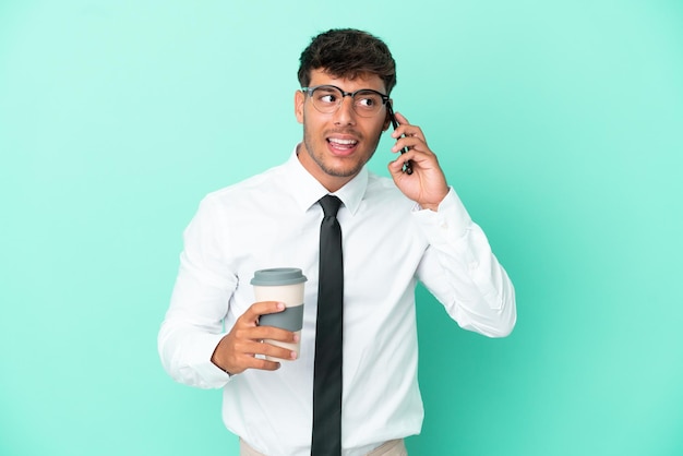 Homem de negócios, caucasiano, isolado em um fundo azul, segurando um café para levar e um celular