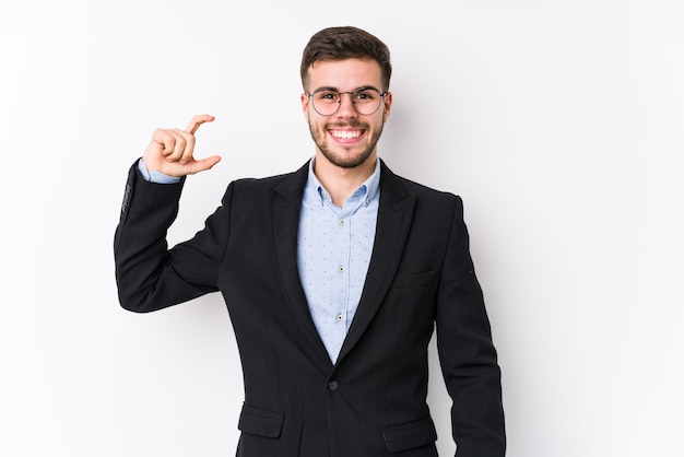 Homem de negócios caucasiano jovem posando em um fundo branco isolado Homem de negócios caucasiano novo segurando algo pouco com o dedo indicador, sorrindo e confiante.