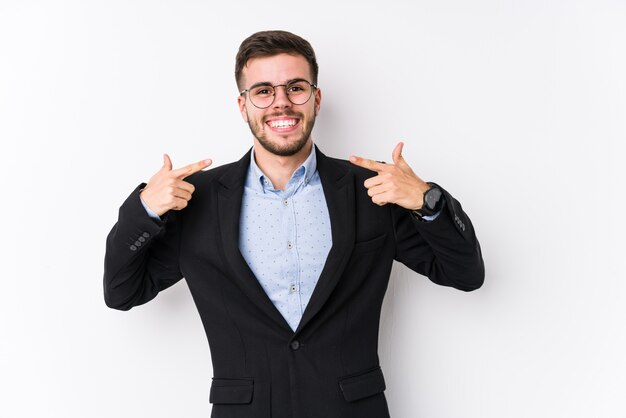 Homem de negócios caucasiano jovem posando em uma parede branca Sorrisos de homem de negócios caucasiano jovem, apontando os dedos na boca.