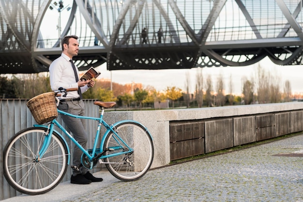 Homem de negócios com bicicleta vintage à beira do rio lendo um livro