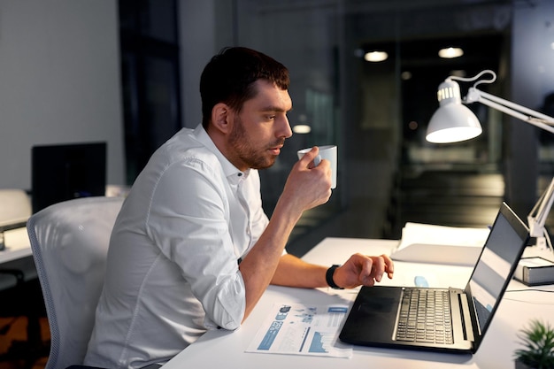 homem de negócios com café e laptop no escritório à noite