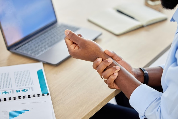 Homem de negócios com dor no pulso e lesão muscular enquanto está sentado na mesa e trabalhando como analista de dados Closeup mão de um empresário masculino negro que sofre de síndrome do túnel do carpo ou artrite no escritório