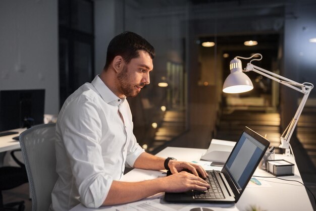 Foto homem de negócios com laptop a trabalhar no escritório à noite