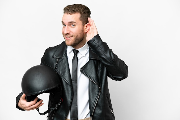 Homem de negócios com um capacete de moto sobre fundo branco isolado, ouvindo algo, colocando a mão na orelha