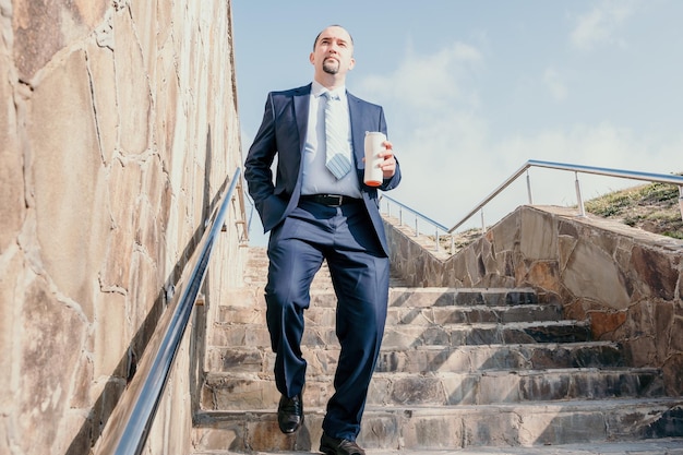 Homem de negócios confiante de meia-idade com uma pasta, andando no andar de cima, close-up do empresário vestindo azul