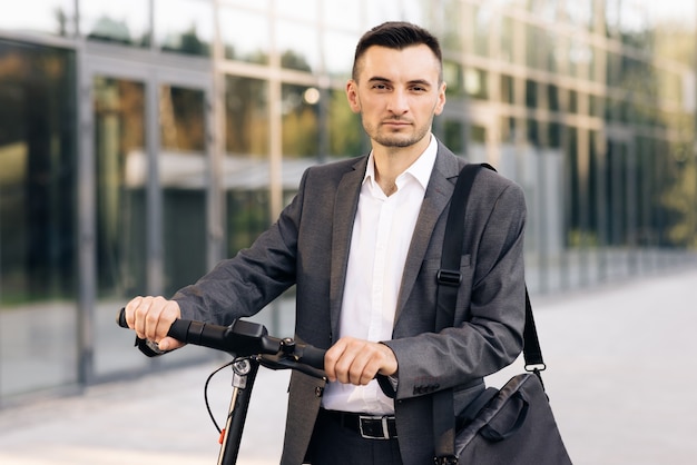 Homem de negócios confiante em pé com uma scooter elétrica e olhando para o aluguel do piloto do escooter da câmera