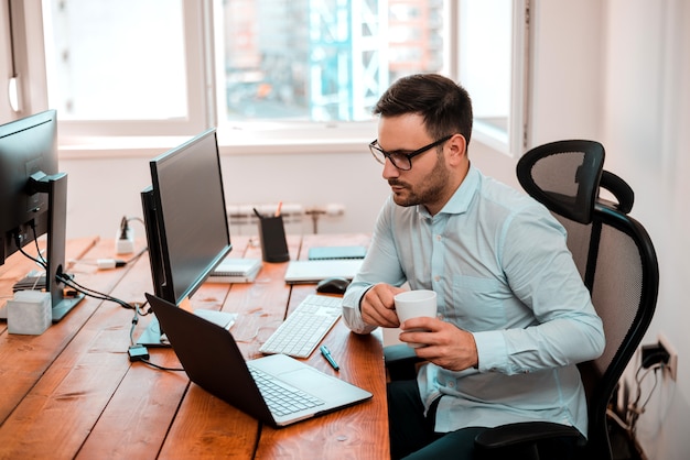 Foto homem de negócios considerável novo em seu portátil que trabalha no escritório moderno.