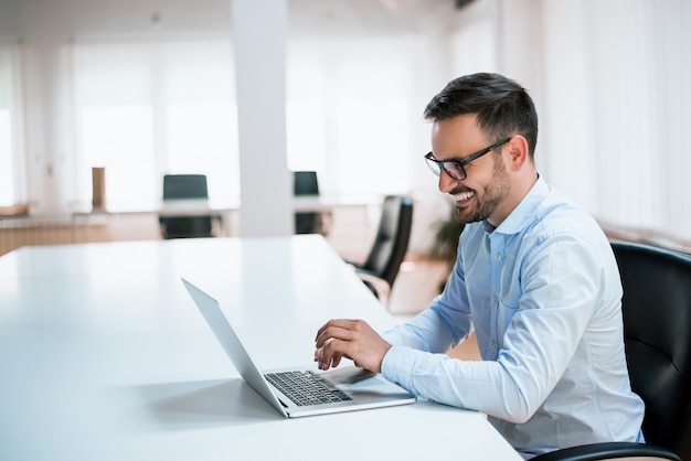 Homem de negócios considerável que trabalha com o portátil no escritório.