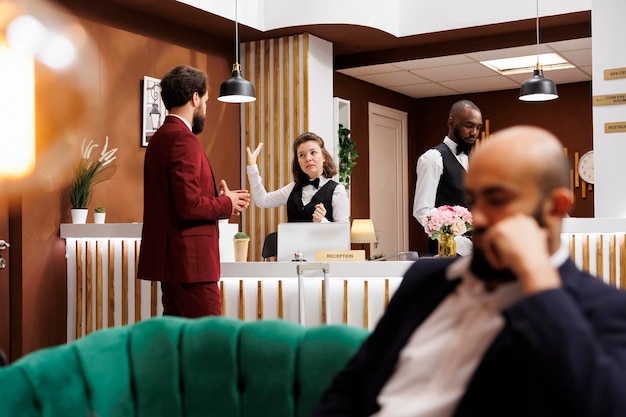 Foto homem de negócios conversa com o pessoal da recepção no saguão da recepção, perguntando sobre os serviços do quarto do hotel depois de fazer o check-in. convidado formal a chegar ao resort, a viajar em viagem de negócios.